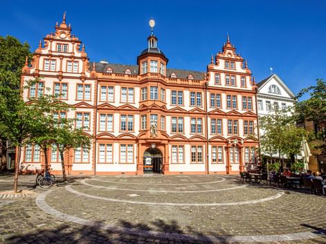 Rot-weißes Gutenberg-Museum in Mainz im Renaissance-Stil mit verzierten Giebeln und zentralem Turm an einem Kopfsteinpflasterplatz.