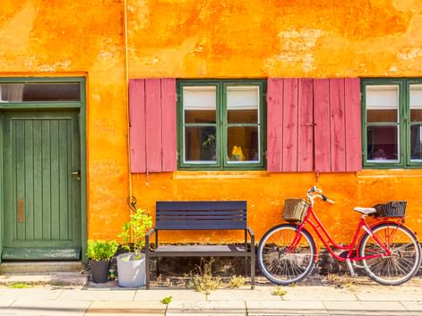 Rotes Fahrrad mit Korb vor gelbem Haus mit grüner Tür und rosa Fensterläden im Kopenhagener Stadtteil Nyboder.
