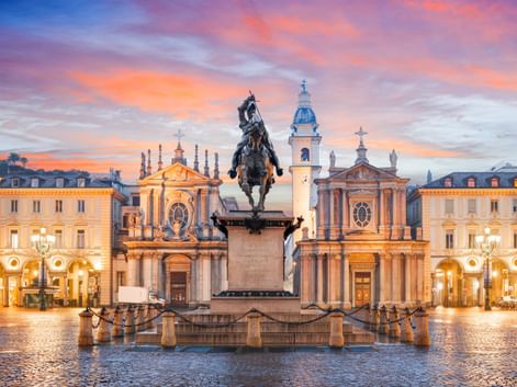 Reiterstandbild in der Mitte der Piazza San Carlo in Turin bei Sonnenuntergang, flankiert von barocken Zwillingskirchen und eleganten Gebäuden.