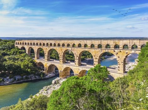 Pont du Gard, antikes römisches Aquädukt mit drei Bogenreihen über einem Flusstal, umgeben von grünen Bäumen unter blauem Himmel.