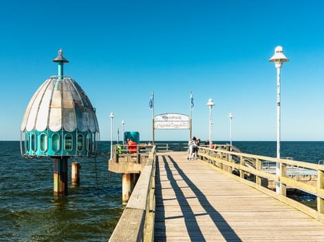 Hölzerne Seebrücke in Zinnowitz, die in die Ostsee führt, mit einer markanten türkis-weißen Tauchgondel auf der linken Seite.