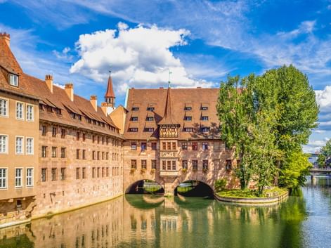 Historisches Heilig-Geist-Spital mit Bogenbrücke über die Pegnitz in Nürnberg, umgeben von traditionellen Gebäuden und Bäumen.