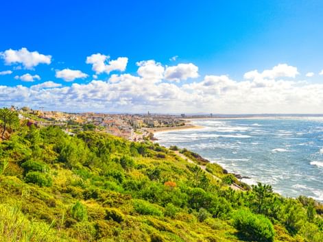 Panoramablick auf die Küste von Figueira da Foz mit grünem Hang, Sandstrand und Atlantik unter blauem Himmel mit weißen Wolken.