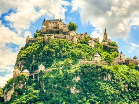 Burg Hochosterwitz auf einem steilen, bewaldeten Hügel in Österreich mit Verteidigungsmauern, Türmen und Kirchturm unter bewölktem Himmel.