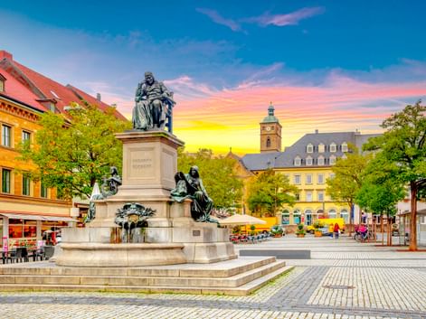 Historic market square in Schweinfurt with monument, colorful buildings, church tower, and cobblestone pavement under a vibrant sunset sky.