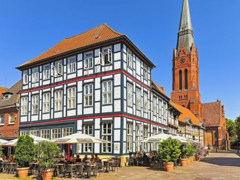 Historic market square in Nienburg with white half-timbered building and outdoor café. Red brick church with tall spire stands behind.