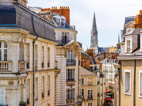 Blick auf historische französische Architektur in Nantes mit cremefarbenen Gebäuden, Schieferdächern und einem Kirchturm im Hintergrund.