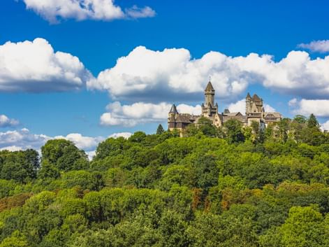 Schloss Braunfels mit Türmen thront auf einem dicht bewaldeten Hügel unter blauem Himmel mit weißen Wolken in Westdeutschland.