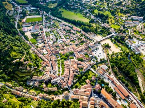 Luftaufnahme von Lamastre, einer französischen Stadt in der Ardèche mit roten Ziegeldächern, umgeben von grünen Feldern und Wäldern mit Fluss.
