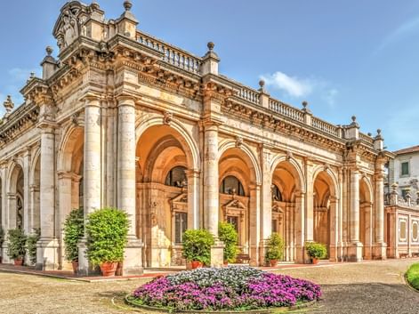 Neoklassizistisches Gebäude mit Bogenkolonnade in Montecatini Terme. Verzierte Balustraden krönen die Struktur. Bunte Blumenbeete schmücken den Hof.