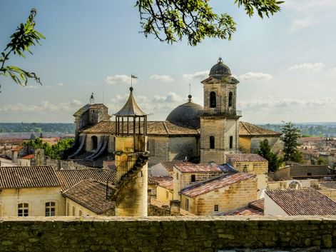 Blick auf eine historische Kirche mit Kuppel und Glockenturm in Beaucaire, umgeben von Steingebäuden mit Terrakottadächern unter blauem Himmel.