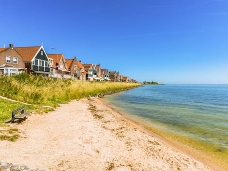 Sandstrand in Volendam mit traditionellen niederländischen Häusern mit orangen Ziegeldächern entlang der Küste. Klarer blauer Himmel.