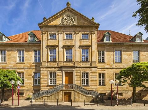 Barockes Sandsteingebäude mit verziertem Giebel und doppelter Freitreppe in Osnabrück. Die Bischöfliche Kanzlei hat ein rotes Ziegeldach.