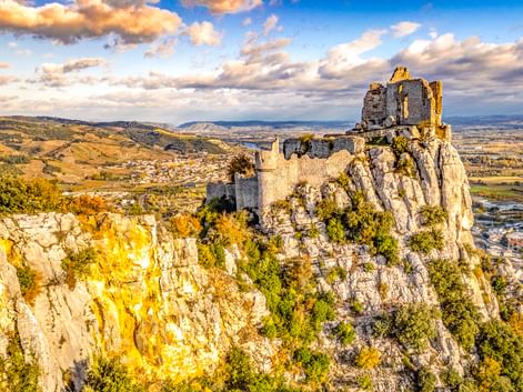 Mittelalterliche Ruine des Château de Crussol auf einem Felsen bei Valence, Frankreich. Steinmauern krönen den Gipfel mit Talblick unter blauem Himmel.
