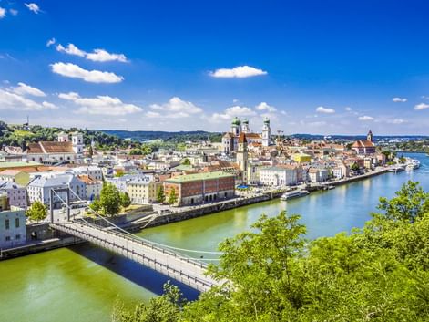 Panoramablick auf Passaus historische Altstadt an der Donau mit bunten Gebäuden, Kirchtürmen und einer Brücke unter blauem Himmel.