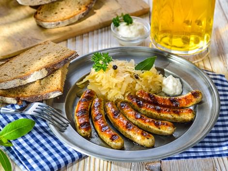 Teller mit gegrillten Würstchen, Sauerkraut und Brotscheiben auf einem Holztisch, begleitet von einem Glas Bier in Franken.