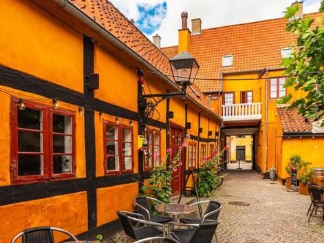 Enge Kopfsteinpflastergasse in Køge mit leuchtend orangen Fachwerkhäusern, rotgerahmten Fenstern, orangen Ziegeldächern und Café-Bestuhlung.
