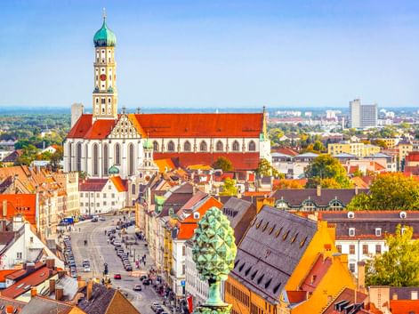 Luftaufnahme der Basilika St. Ulrich und Afra mit markanter grüner Zwiebelkuppel und rotem Dach, die Augsburgs historische Altstadt überragt.