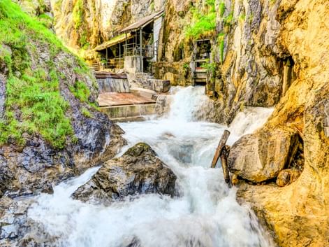 Rauschender Wasserfall in enger Felsschlucht mit moosbewachsenen Wänden und Holzstegen im Zammer Lochputz in Österreich.