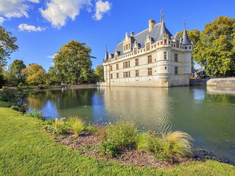 Château d'Azay-le-Rideau, ein weißes Renaissance-Schloss mit Türmchen und Schieferdach, spiegelt sich im umgebenden Wassergraben unter blauem Himmel.