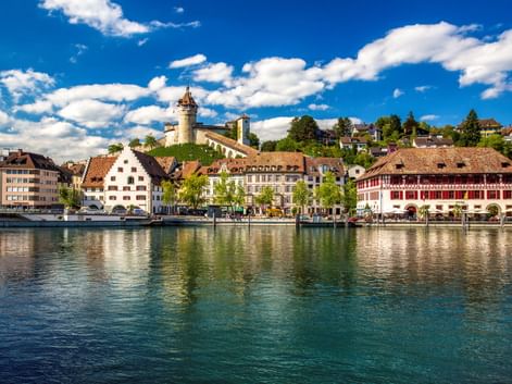 Blick auf Schaffhausen am Rhein mit historischen Gebäuden und der Festung Munot auf dem Hügel. Traditionelle Schweizer Architektur spiegelt sich im Rhein.