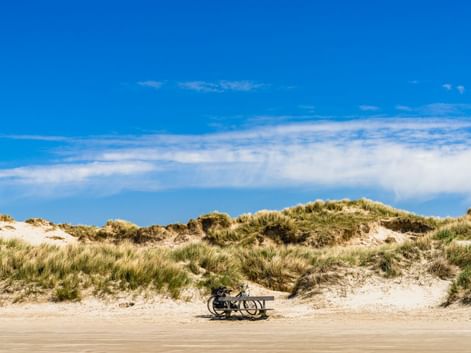 Fahrrad auf einem breiten Sandstrand mit grasbewachsenen Dünen unter blauem Himmel mit weißen Wolken in Belgien.