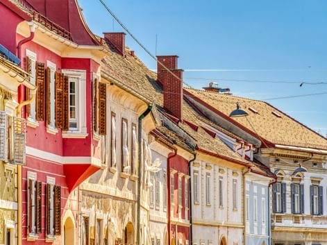 Row of historic buildings with colorful facades in pink, yellow, and white in Bad Radkersburg under blue sky with traditional tiled roofs.