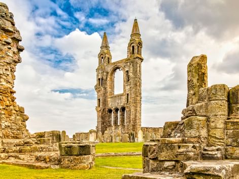 Steinruinen der St Andrews Kathedrale mit hohem gotischem Turm mit zwei Türmen und Bogenfenstern, umgeben von bröckelnden Mauern und grünem Gras.