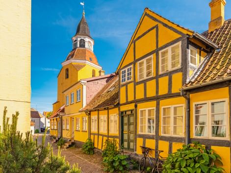 Gelbe Fachwerkhäuser mit Kirchenglockenturm in Faaborg, Dänemark. Die historischen Gebäude zeigen traditionelle Architektur unter blauem Himmel.