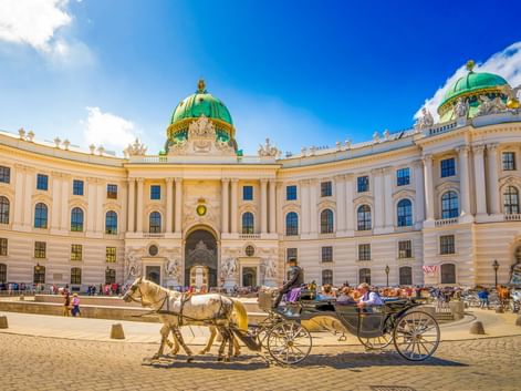 Traditioneller Fiaker im Innenhof der Wiener Hofburg mit ihrer markanten grünen Kuppel und cremefarbenen Barockfassade.