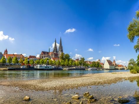 Panoramablick auf Regensburgs historische Skyline mit den Domtürmen über bunten Gebäuden entlang der Donau.