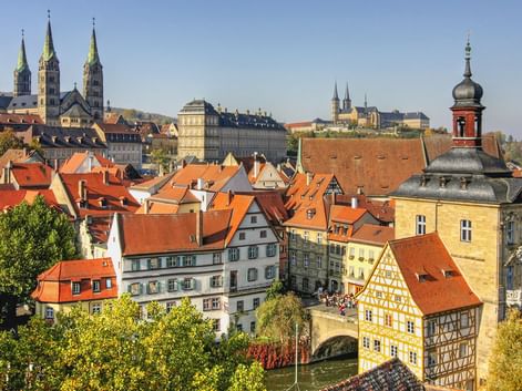 Panoramablick auf Bambergs Altstadt mit roten Ziegeldächern, historischen Fachwerkhäusern, Kirchtürmen und dem Alten Rathaus am Fluss.