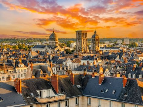 Luftaufnahme von Tours bei Sonnenuntergang mit den Türmen von Saint-Martin-de-Tours über den Dächern. Dramatischer orange-violetter Himmel beleuchtet die Altstadt.