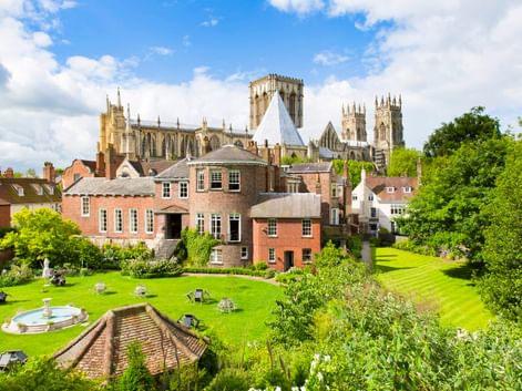 York Minster Kathedrale mit ihren gotischen Türmen erhebt sich über historischen Backsteingebäuden und gepflegten Gärten mit grünen Rasenflächen.