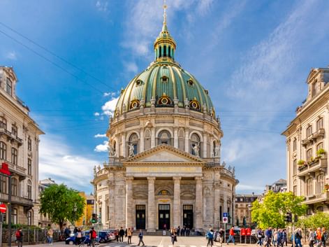 Frederikskirche in Kopenhagen mit markanter grüner Kupferkuppel und goldener Spitze. Die barocke Marmorkirche ist von historischen Gebäuden und Besuchern umgeben.