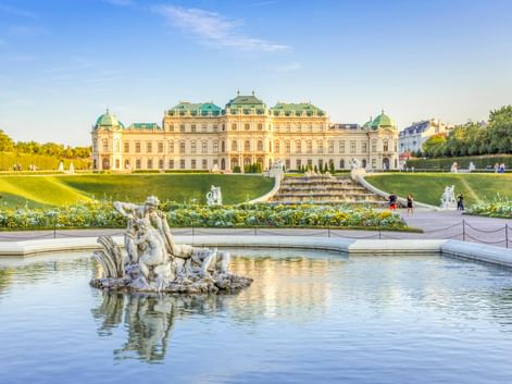 Barockes Schloss Belvedere in Wien mit verziertem Brunnenskulptur im Vordergrund, gepflegten Gärten und türkisfarbenen Kuppeldächern.