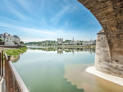 Blick unter einem Steinbrückenbogen auf die Loire in Saumur, mit historischen Gebäuden und Kirchtürmen, die sich im ruhigen Wasser spiegeln.
