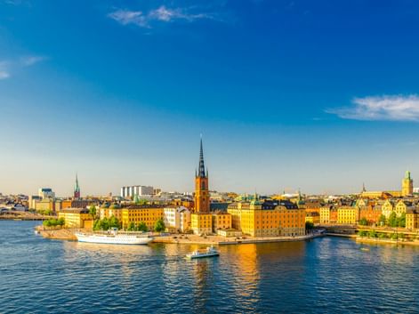 Panoramablick auf Stockholms Gamla Stan mit bunten historischen Gebäuden am Wasser und Kirchtürmen unter blauem Himmel.