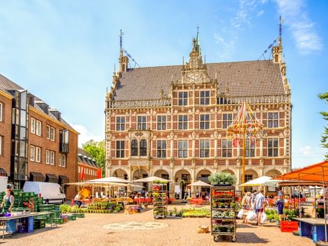 Prachtvolles Renaissance-Rathaus in Bocholt mit Arkadengang im Erdgeschoss und dekorativer Fassade. Marktstände mit orangen Markisen füllen den Platz.