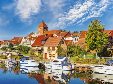Hafen mit weißen Booten in Plau am See. Historische Stadt mit roten Ziegeldächern und Kirchturm unter blauem Himmel mit weißen Wolken.