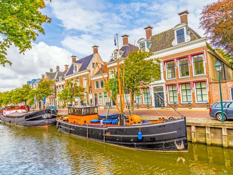 Traditionelle niederländische Boote am Kanal in Harlingen, gesäumt von bunten historischen Gebäuden mit Schornsteinen unter blauem Himmel.