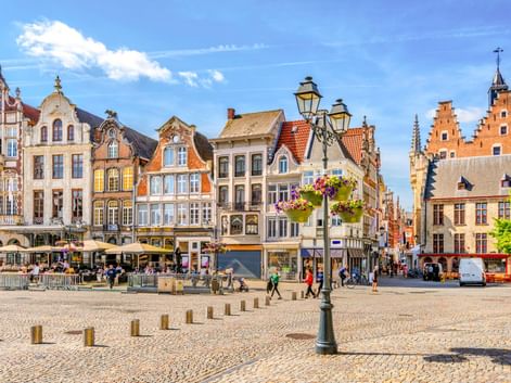 Grote Markt in Mechelen mit bunten historischen Giebelhäusern, Kopfsteinpflaster, verzierter Straßenlaterne mit Blumen und Fußgängern.