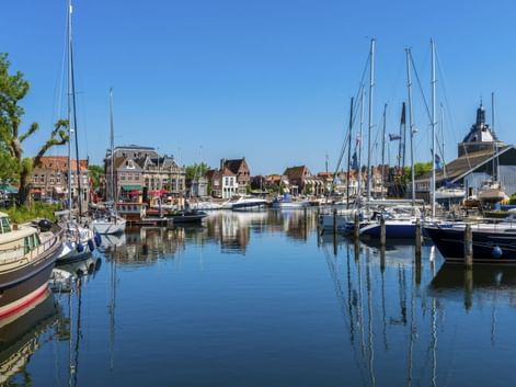 Hafen in Enkhuizen mit Segelbooten am ruhigen Wasser. Historische Gebäude und ein Kirchturm säumen die Uferpromenade unter blauem Himmel.