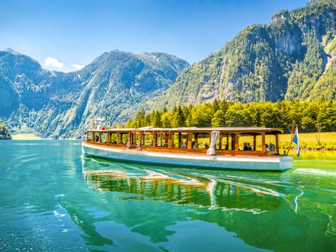 Traditionelles Passagierboot mit Holzkabine auf dem klaren grünen Wasser des Königssees, umgeben von steilen bewaldeten Bergen in Bayern.