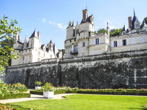 Schloss Ussé in Rigny-Ussé mit weißen Steinmauern, Türmchen und Türmen hinter einer verwitterten Terrassenmauer. Gepflegter Rasen und Gärten im Vordergrund.