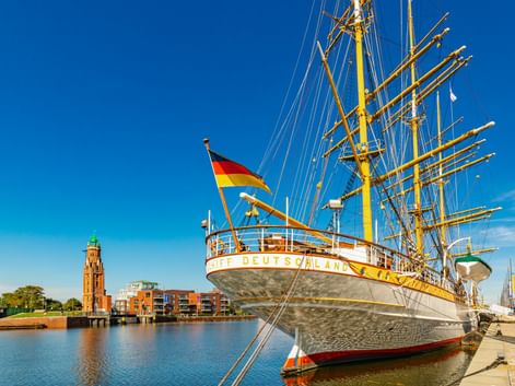 Weißes Segelschiff Deutschland mit deutscher Flagge am Neuen Hafen in Bremerhaven. Roter Backsteinleuchtturm und moderne Gebäude am Wasser.