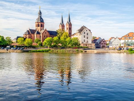 Blick über den Main auf Seligenstadt mit der Einhardsbasilika mit Zwillingstürmen und Kuppel, umgeben von historischen Gebäuden.