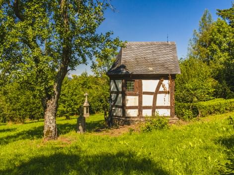Kleine Fachwerkkapelle mit weißen Wänden und braunen Holzbalken im Freilichtmuseum Roscheider Hof in Konz, umgeben von grüner Wiese und Bäumen.