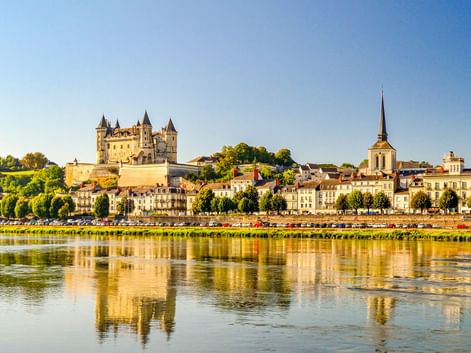 Schloss Saumur mit Türmen auf einem Hügel über der Stadt Saumur und der Loire. Das Schloss und die Gebäude spiegeln sich im Wasser.