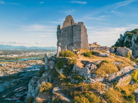 Mittelalterliche Steinruinen der Burg Crussol auf einem felsigen Hügel mit Blick auf Valence und das Rhônetal mit Bergen in der Ferne.